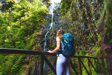 Sportive tourist with backpack leans against wooden fence of viewpoint and watches green overgrown...
