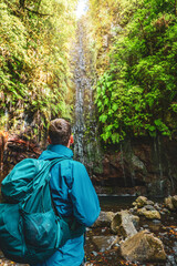 Male toursit with backpack enjoys watching green overgrown waterfall. 25 Fontes waterfalls, Madeira...