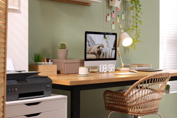 Stylish workplace with computer, laptop and lamp near olive wall at home