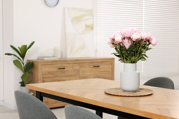 Vase with pink peonies on wooden table in dining room