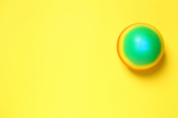 New bright kids' ball on yellow background, top view. Space for text