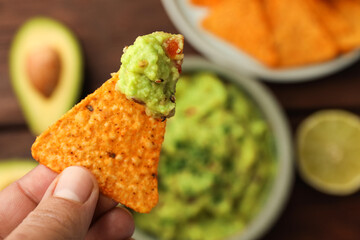 Woman holding delicious nachos chip with guacamole at table, closeup. Space for text