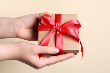 Woman holding gift box with red bow on beige background, closeup