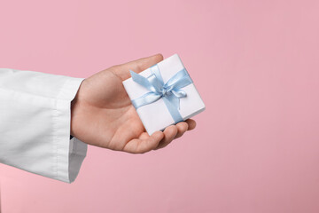 Doctor holding gift box on pink background, closeup. Medical present