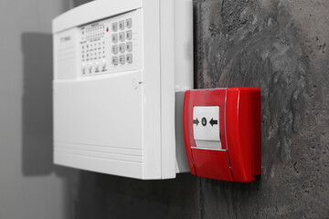 Fire alarm push button and house security system control panel on grey wall