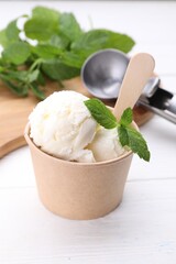 Delicious vanilla ice cream and mint in paper cup on white wooden table
