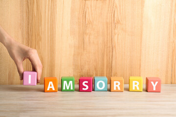 Woman adding cube with letter I to make phrase I Am Sorry at wooden table, closeup. Space for text