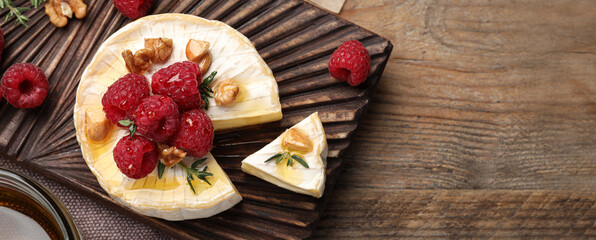 Tasty brie cheese with raspberries, walnuts and honey on wooden table, top view. Banner design with...