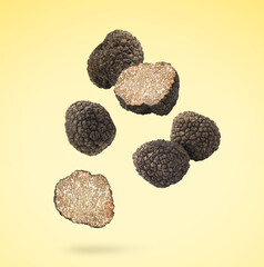 Cut and whole truffles falling on light yellow background