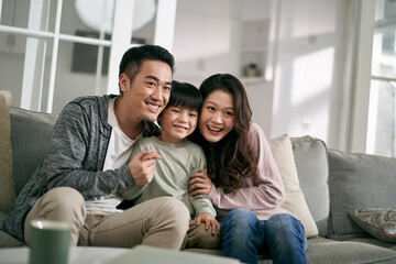 young asian family sitting on couch at home having a good time