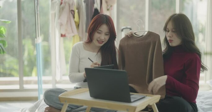 Roommate concept of 4k Resolution. A couple of Asian women helping each other sell clothes online using a laptop at home.