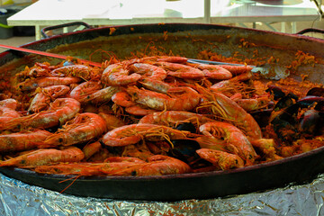 Street food in France, fresh prepared colorful paella with rice and sea food in big pan on street market, ready to eat