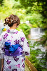 Back view of one woman wearing Japanese yukata summer kimono walking on the road next to the forest...
