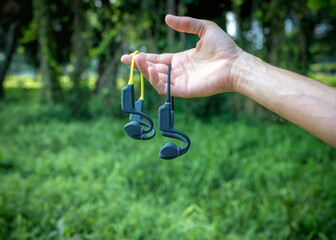 Two pairs of bone conduction sports headphones. Hand holding audio devices on green background.