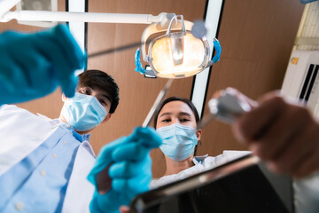 Asian female dentist adjusting surgical light looking from above at patient.