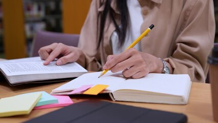 Asian women student sits in library, prepare for exam and making notes in notebook preparing for college test and finding information with a serious face in college library. - Powered by Adobe