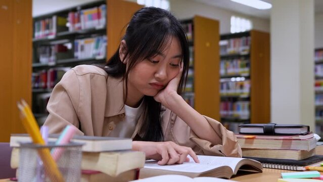 Anxious young Asian woman with hand on head feeling tired and stressed while read books about her homework in library at university