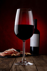 Promotional shot of glass, bottle of red wine with empty label and jamon serrano on rusty brown background. Mockup, frontal view