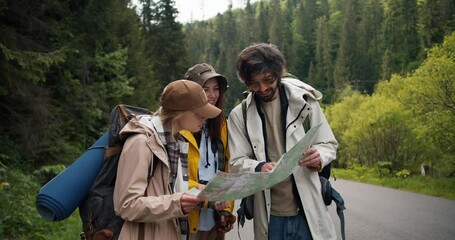 A trio of tourists get lost and are looking at a map to figure out where to go next. People in hiking clothes sort out where to have next in mountainous terrain