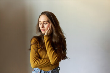 Pretty stylish woman of 20s touching gently cheek posing against gray copy space background, having long thick beautiful, well-conditioned hair. Haircare products and procedures concept