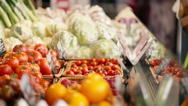 Close-up shot of a Black man in a plaid shirt choosing vegetables at a supermarket counter. View of juicy and rich summer vegetables. Video filmed in high quality
