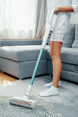 A young woman cleans the house with a vacuum cleaner. Upright vacuum cleaner cordless. Battery...
