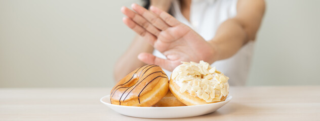Diet concept, asian young woman hand push out, deny sugar donut, doughnut and sweet taste food on plate, fighting to keep it from getting fat when person bring to me. Healthy nutrition of weight loss.