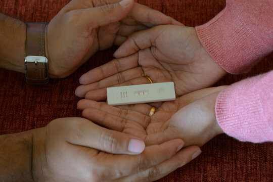 Hands of a couple protecting home pregnancy test kit showing positive results. Fertility, conception, missed periods, baby, womb, mother, gynaecologist, pregnant, sex