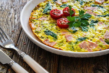 Delicious breakfast - egg omelette with mortadella, leek,spinach and cherry tomatoes on wooden table
