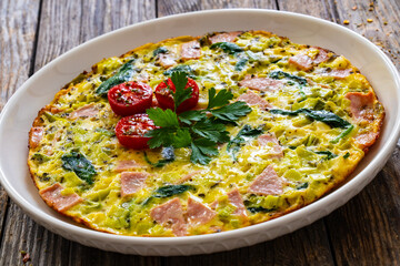 Delicious breakfast - egg omelette with mortadella, leek,spinach and cherry tomatoes on wooden table
