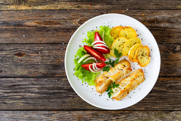 Seared cod loin with fried potatoes and fresh vegetables on wooden table