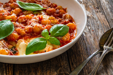 Gnocchi alla sorrentina - gnocchi with melted mozzarella cheese in tomato sauce and  Parmigiano Reggiano on wooden table
