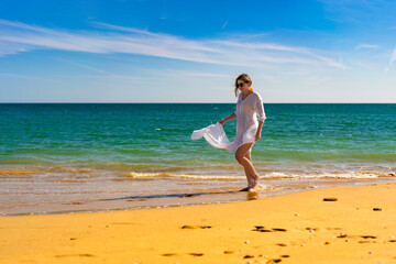 Beautiful woman walking on sunny beach holding shawl
