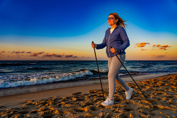 Nordic walking - woman training on beach at sunset
