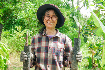 Female farmer happily holding a rubber tree in her hand.
