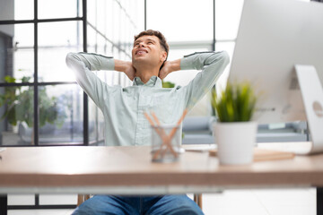 Young modern businessman keeping hands behind head and smiling while sitting in the office.