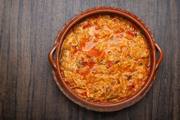 Authentic mexican chicken tinga, typical mexican food prepared in a clay pot on a wooden table.