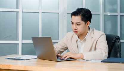 Fototapeta premium Businessman in a light blazer smiles and celebrates in front of his laptop, conveying excitement and success in a professional setting.