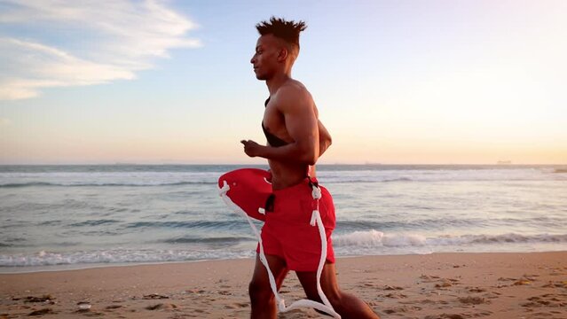 African American lifeguard running along the beach in Southern California at Sunset. Lifeguard's left hand is deformed.