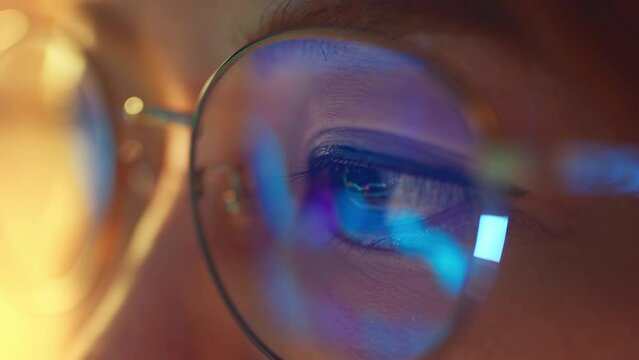 Closeup - Female eyes in eyeglasses late at night scrolling in front of laptop. Coder, she checking Bitcoin price chart on digital exchange on smartphone, cryptocurrency future price action prediction
