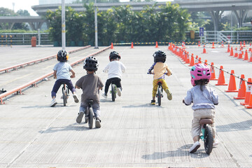 kids from 2-5 years old races on balance bike in a parking area with cones as track, back view, behind view shoot.