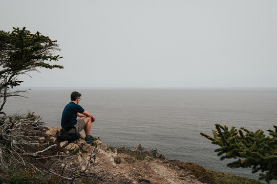 Man sitting on rocky cliff overlooking ocean in Newfoundland.