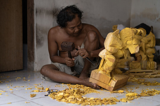 A man carves a statue in wood in workshop. Woodcarving Bali.