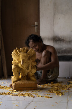A man carves a statue in wood in workshop. Woodcarving Bali.