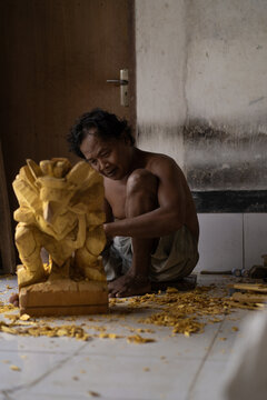 A man carves a statue in wood in workshop. Woodcarving Bali.