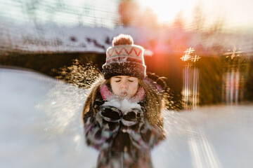 girl blowing snow during winter at sunset