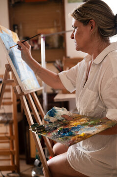 Side view of a mature woman painting a picture in her home.