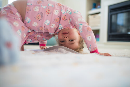 Young girl bend upside down, playing in living room at home.