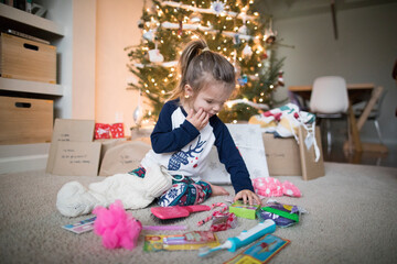young girl spreads her gifts out under the Christmas Tree
