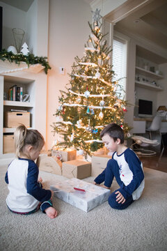 Brother and sister opening gifts together under the tree